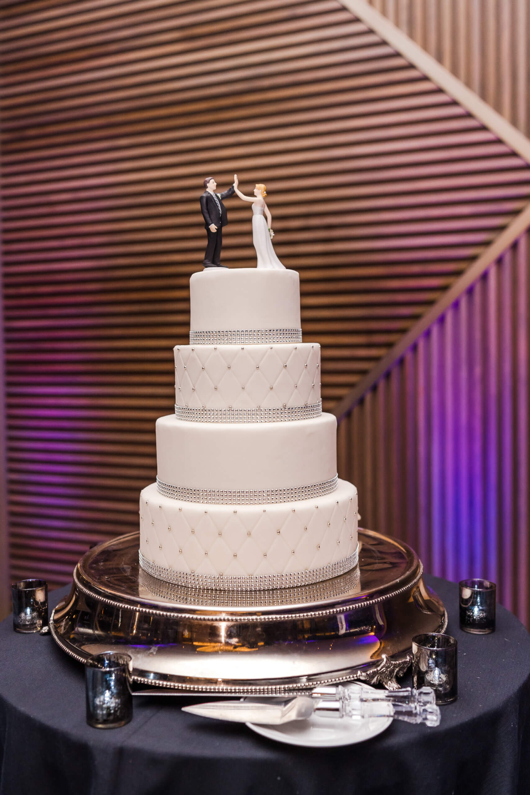 White wedding cake with a couple on top giving a high five.