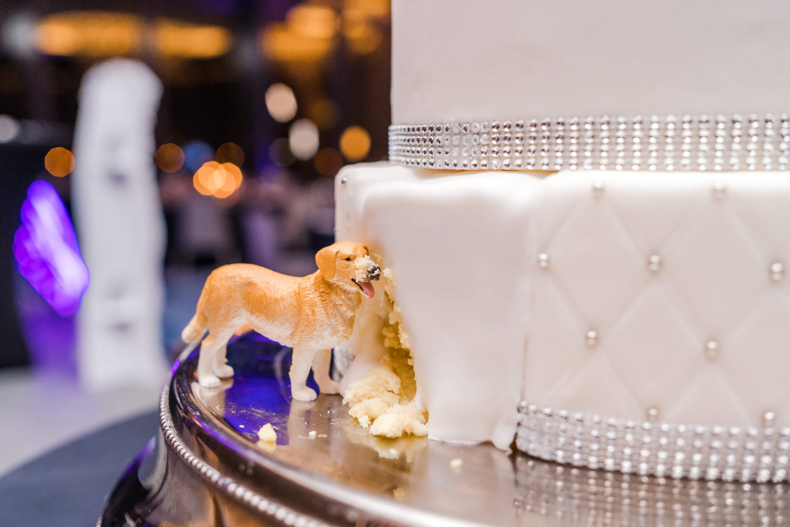 Wedding cake with a small dog statue by it, and it looks as if the dog has eaten part of the cake!